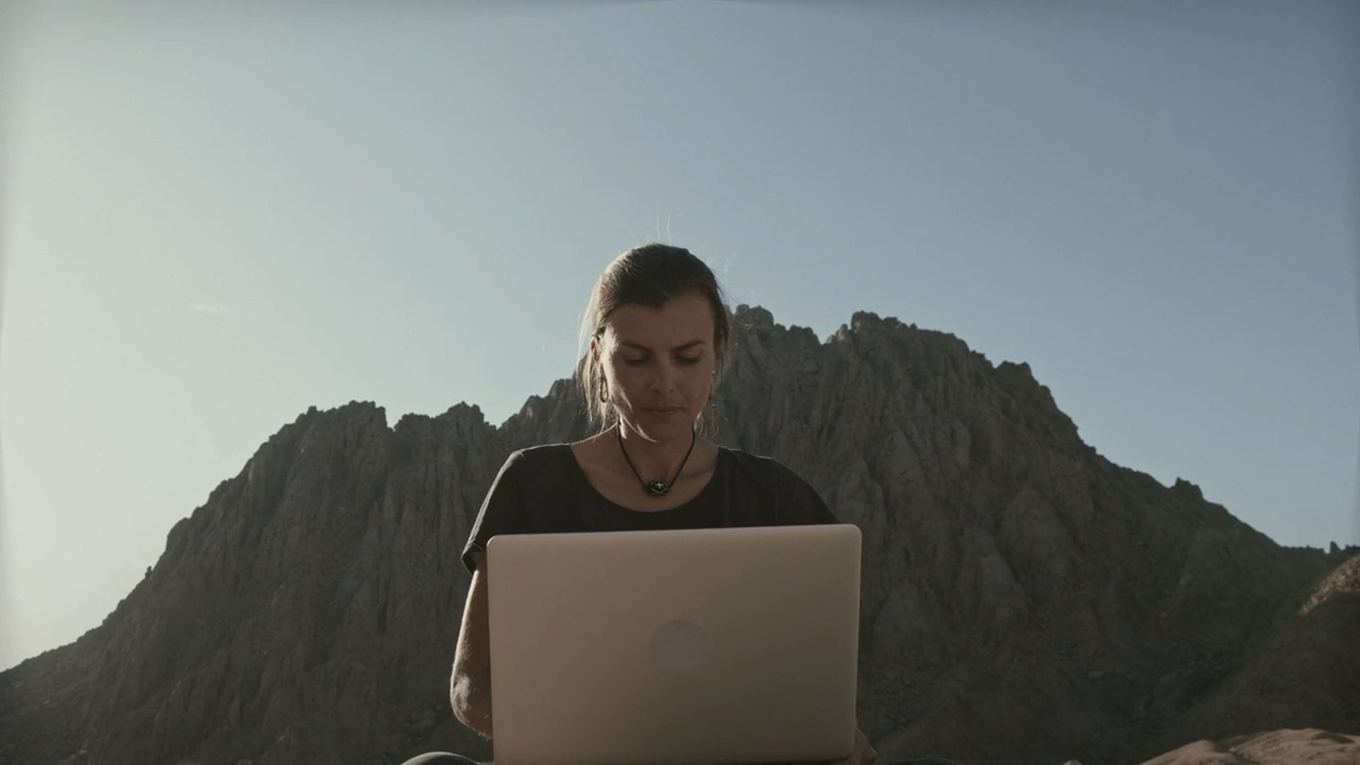 A person working on a laptop with mountains in the distance